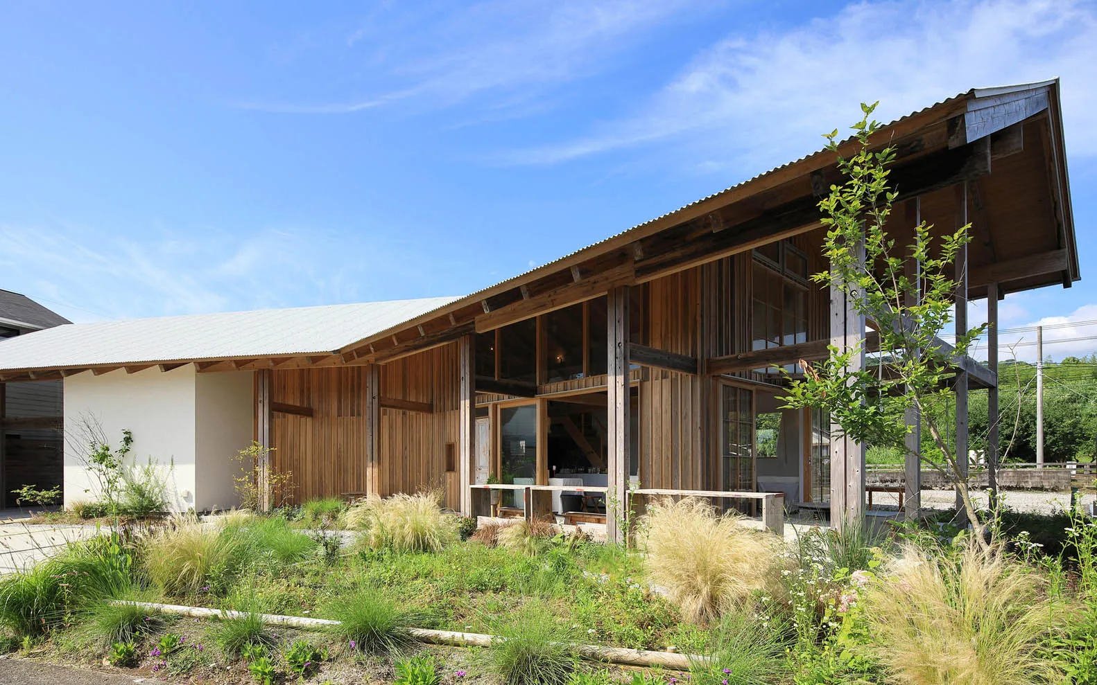 A modern cabin with a wooden exterior, green shrubs in the forground, and a clear blue sky above.