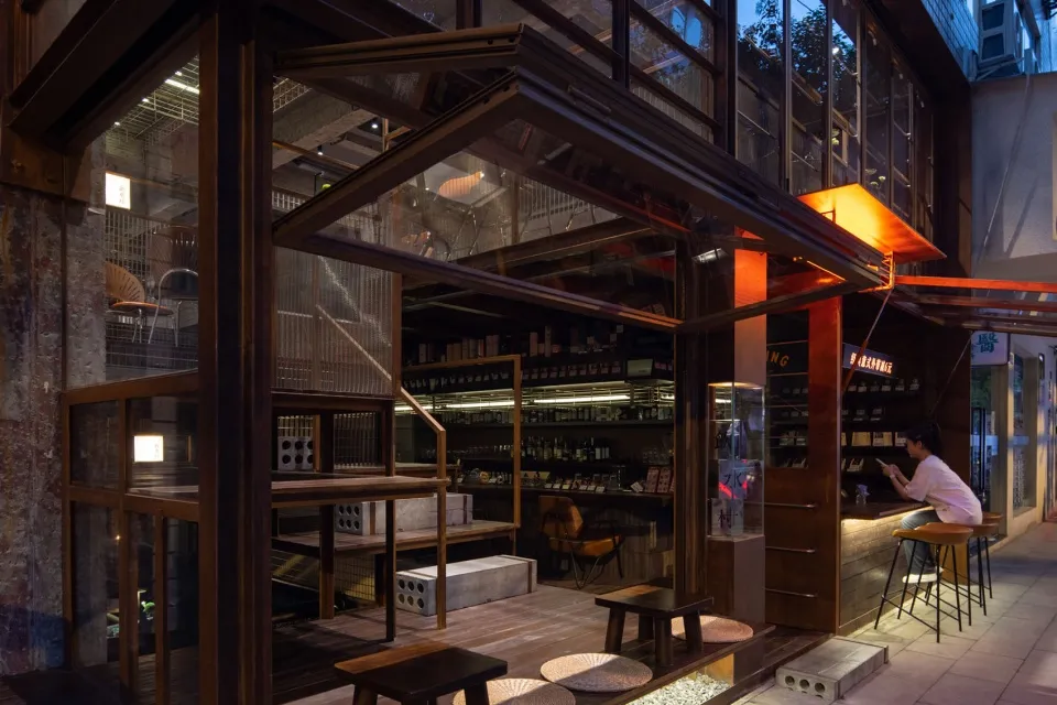 An industrial-style restaurant interior featuring wooden tables, glass shelves, and concrete surfaces.