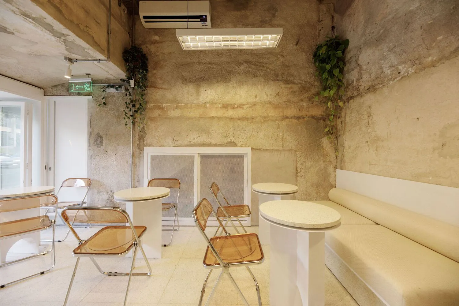 A modern cafe interior with concrete walls, white tables, and orange chairs.