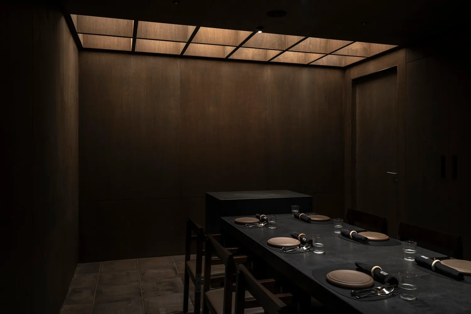 A dimly lit, industrial-themed restaurant interior with a long, dark table set for dining and metallic accents.