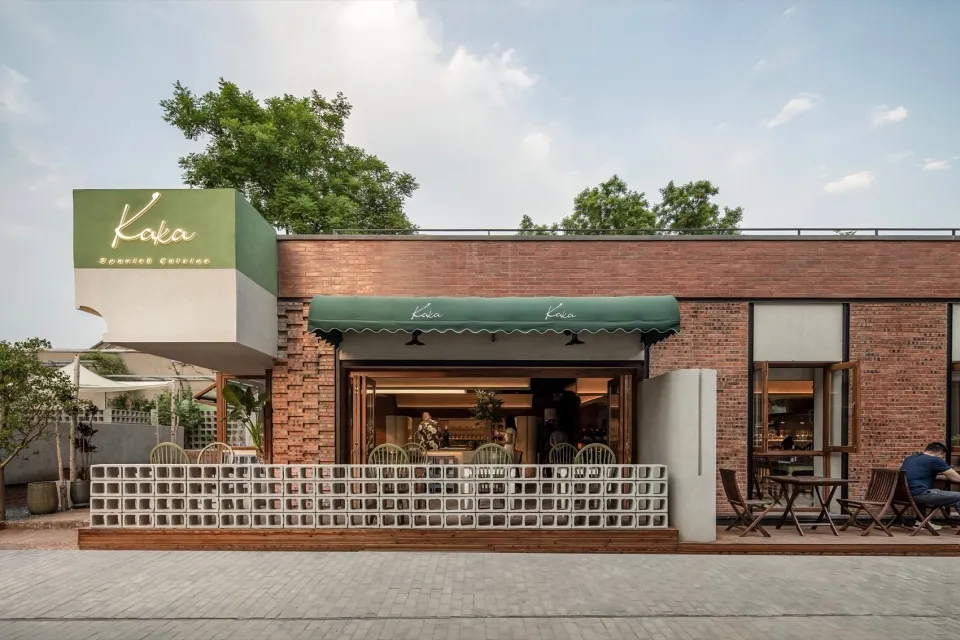A modern restaurant exterior featuring a brick wall and a green awning with the name 'Kaka' on it.