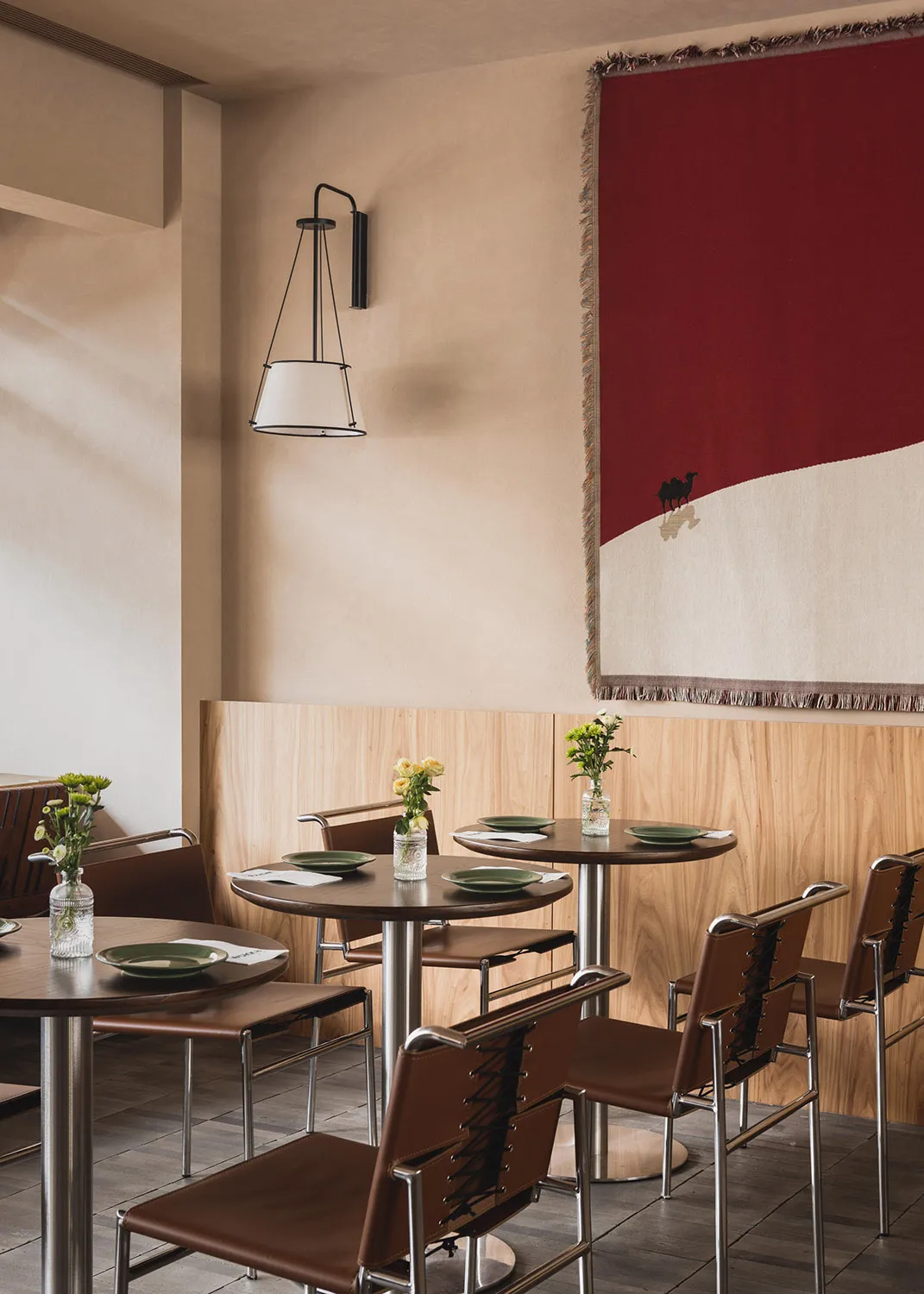 A modern cafe interior featuring a red wall tapestry with a camel design.