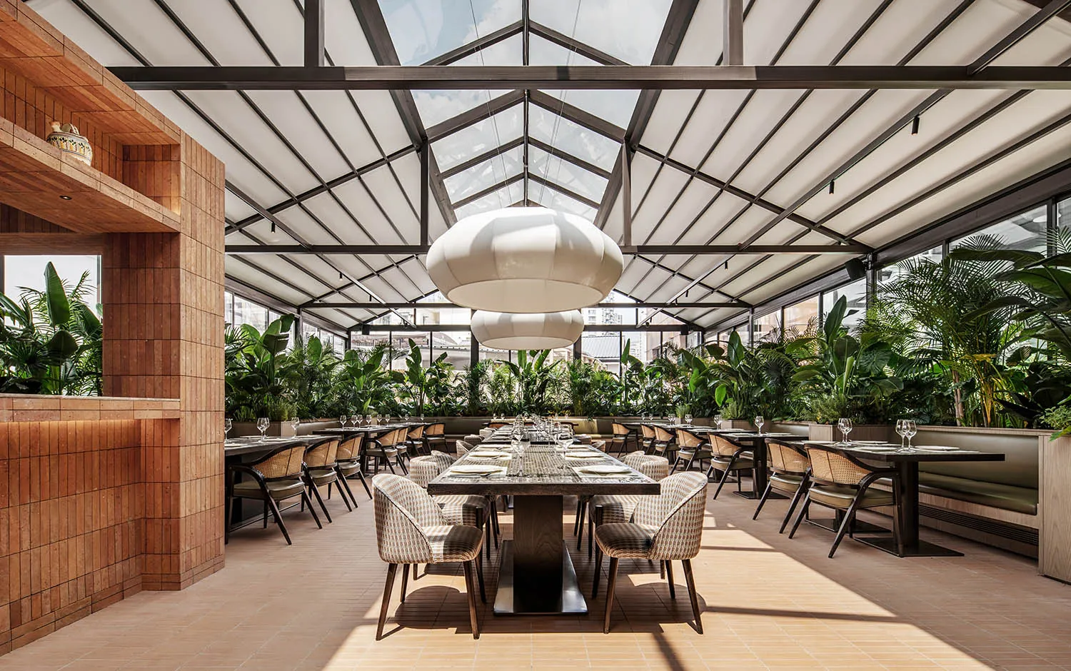 工業風餐廳室內,配有金屬桌椅、玻璃天花板,以及綠色植物。