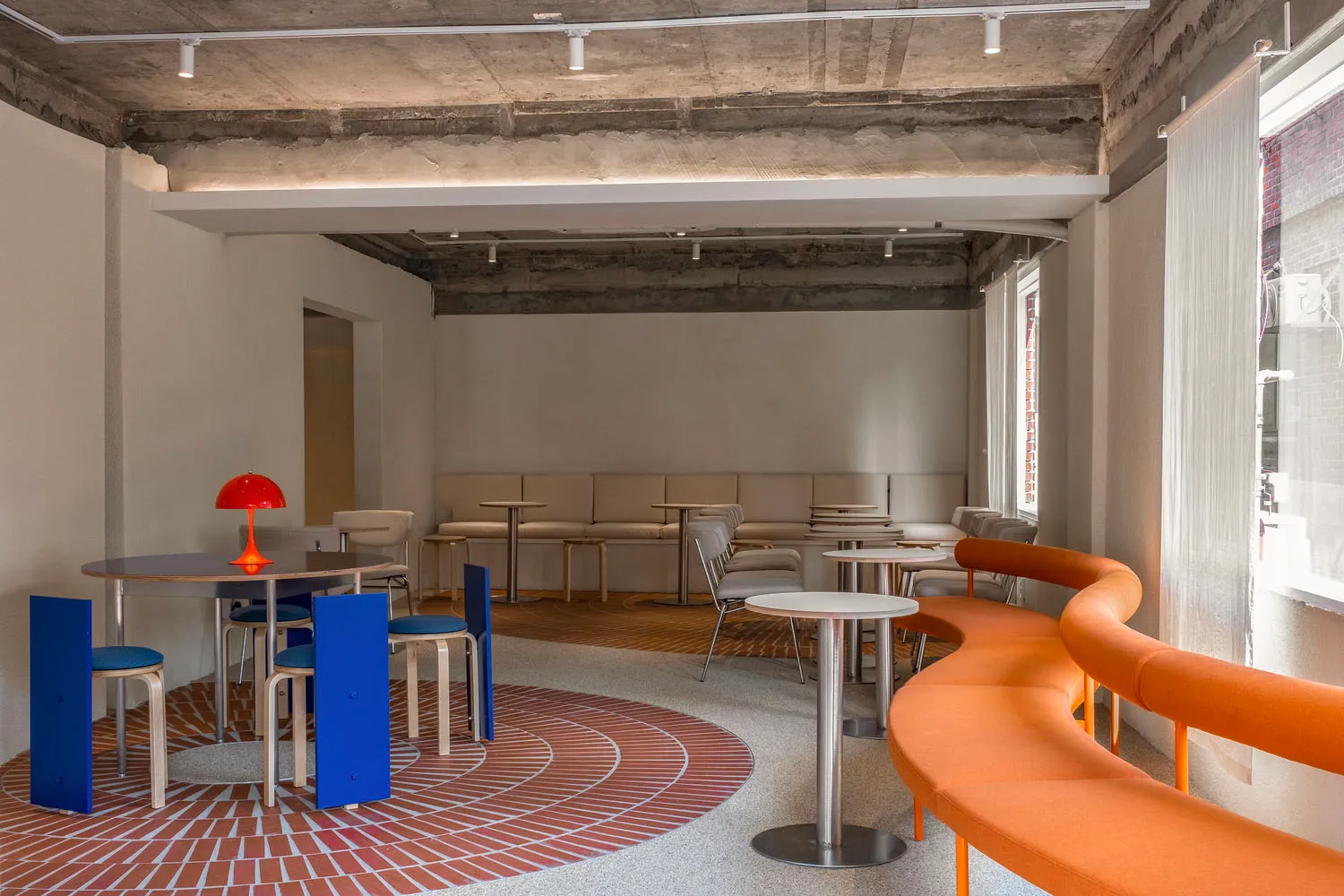 Modern cafeteria with concrete ceiling, brick floor, and fabric seating.