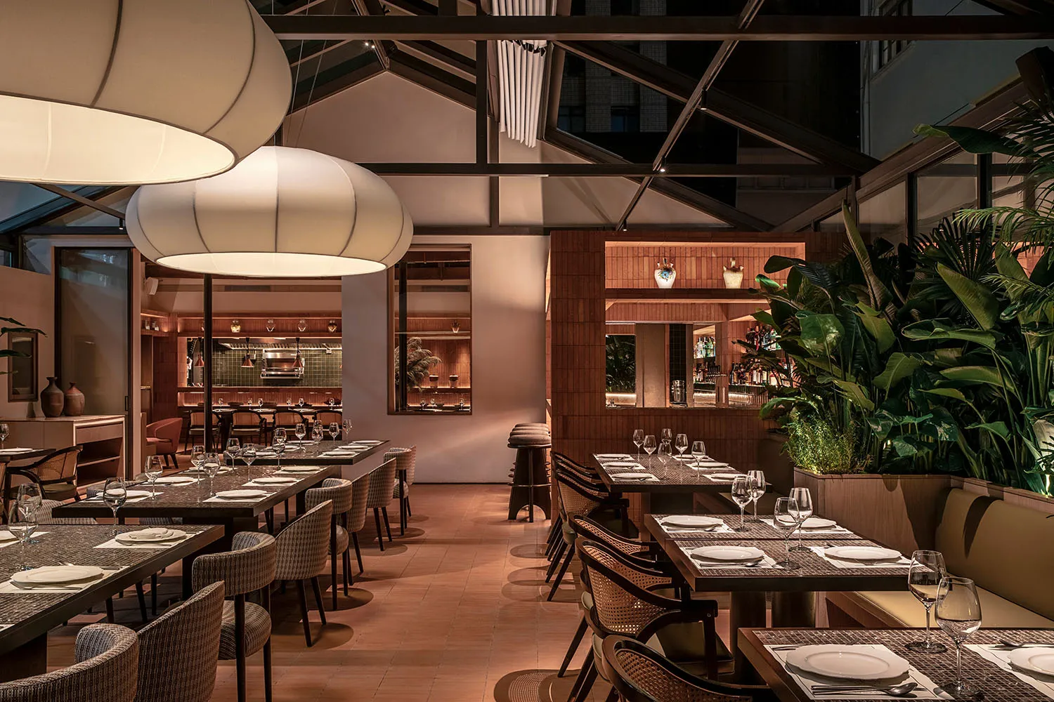 Modern restaurant interior with industrial design elements, featuring wood furniture, glass lighting, and greenery.