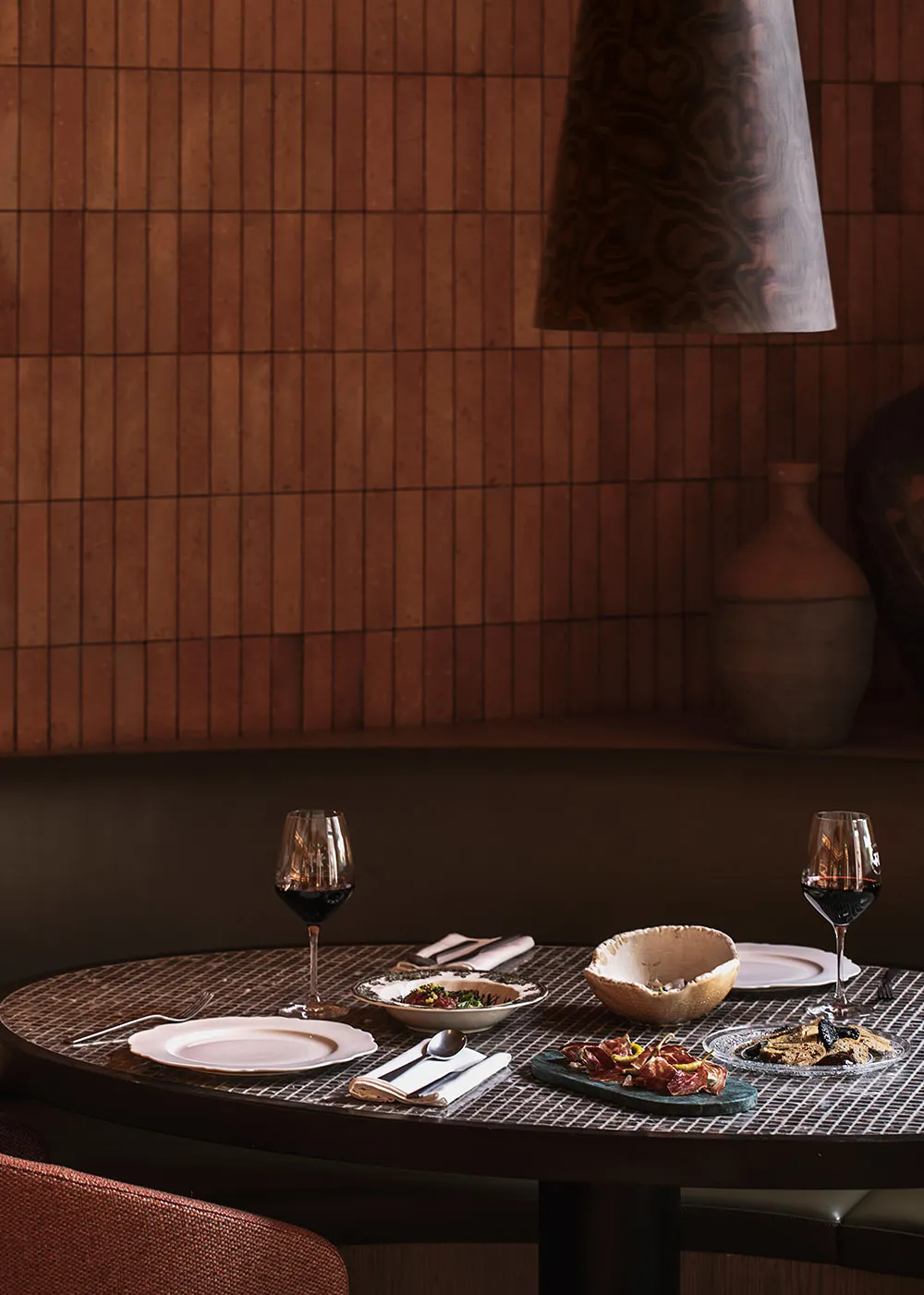 Modern dining room with terracotta tile walls, dark wooden table, and wine glasses.