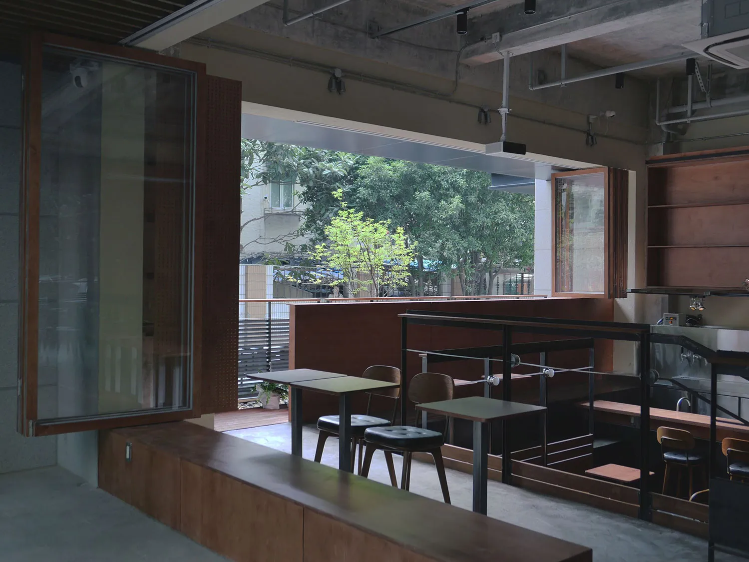現代工業風格咖啡廳室內,搭配木質餐桌、椅與層架,並可眺望戶外綠意。