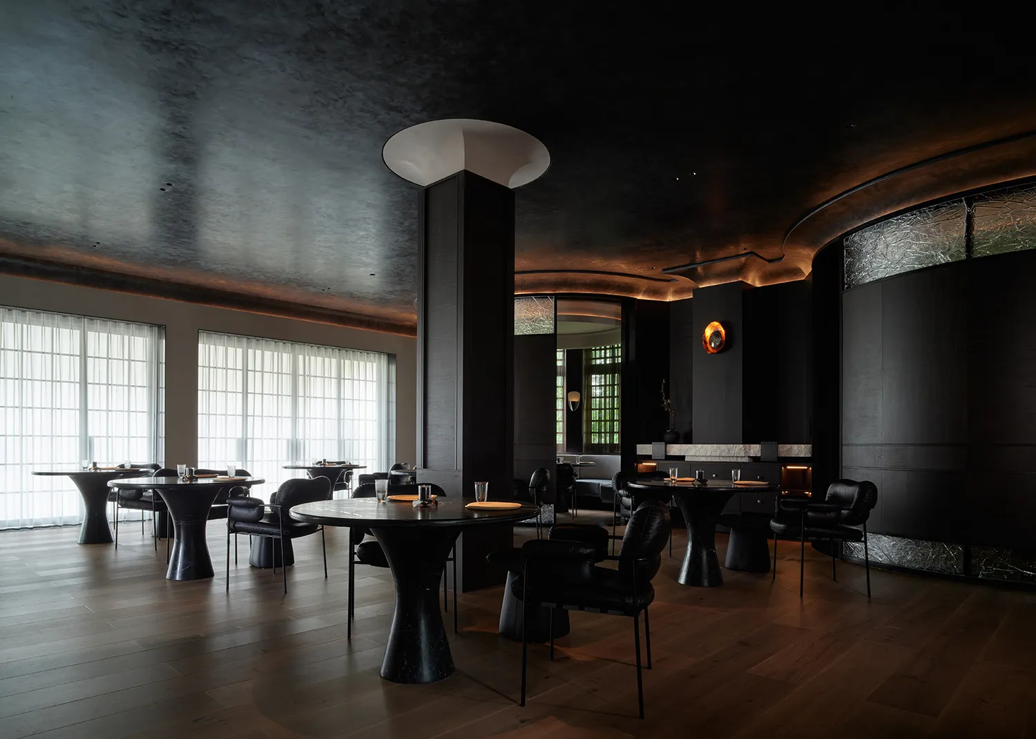 A modern restaurant interior with dark wood, stone, and metal finishes, featuring black tables and minimalist decor.