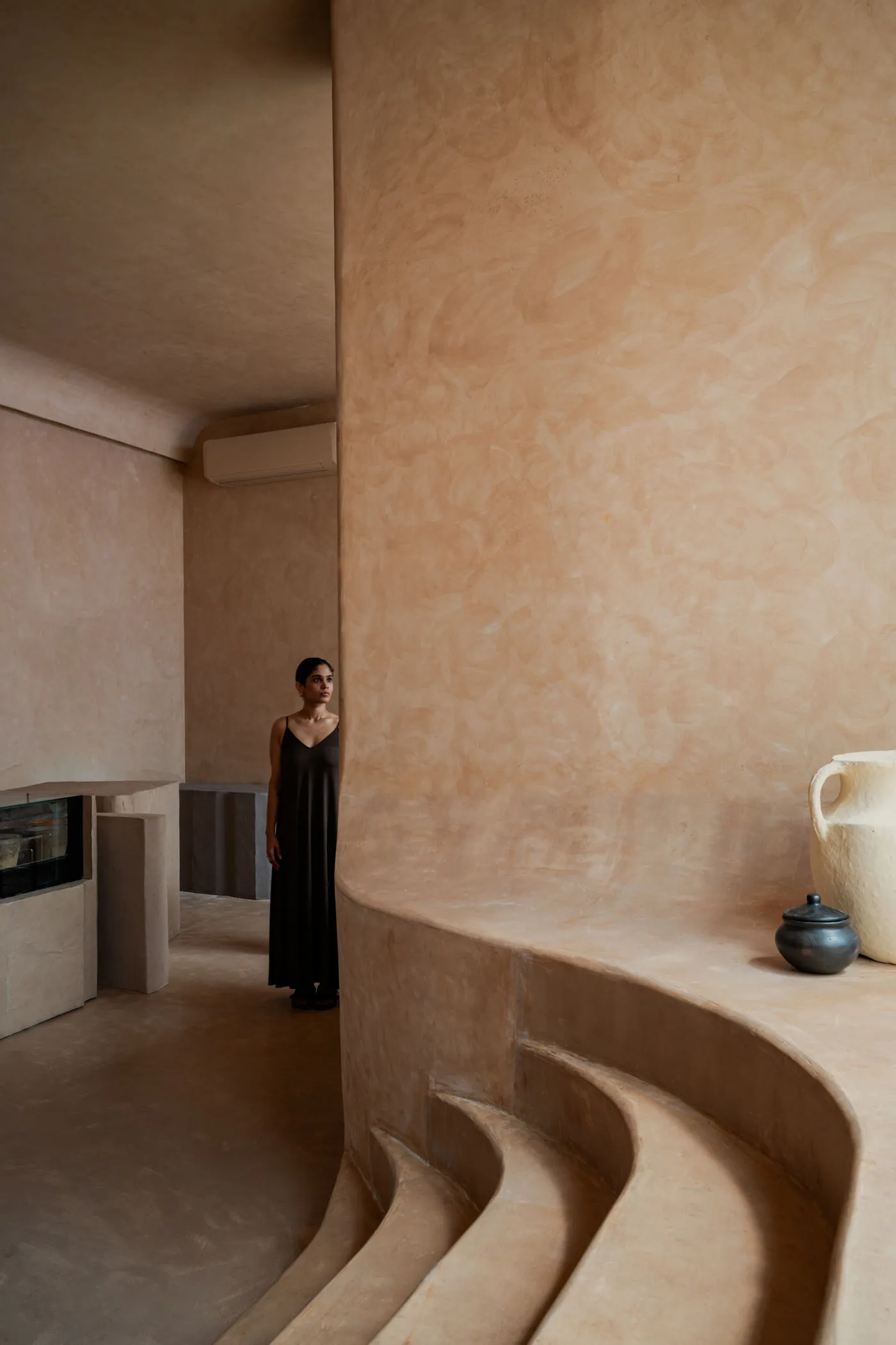 A minimalist interior space featuring concrete walls and steps, with a person standing in the background.