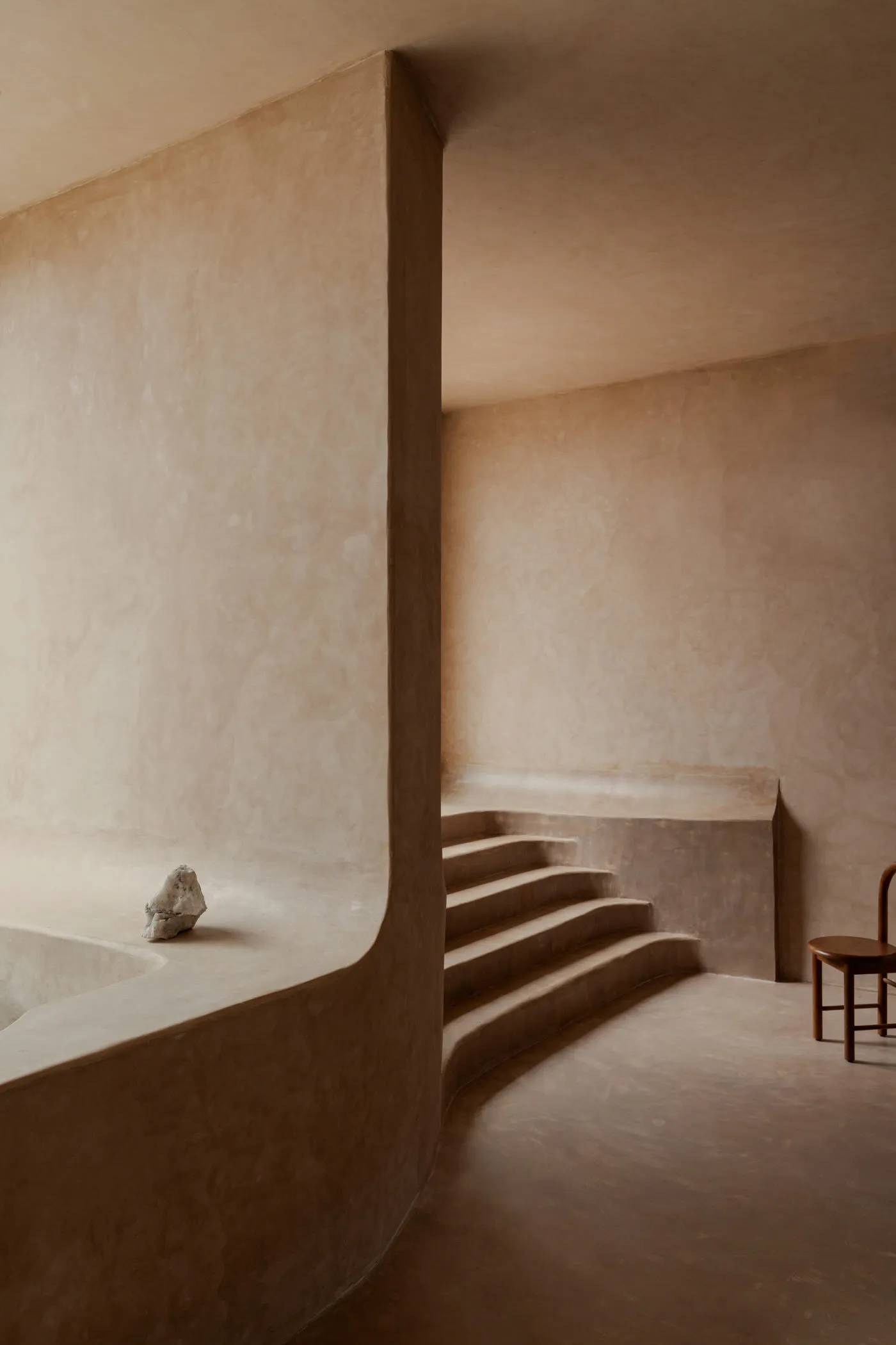 A minimalist modern interior with concrete walls and a wooden chair.