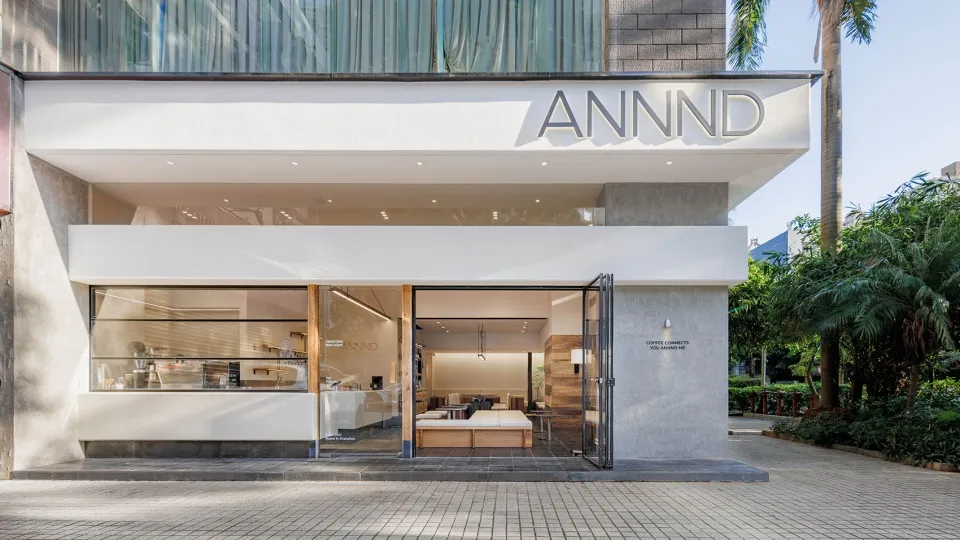 A minimalist coffee shop with large glass windows and concrete exterior, featuring modern furniture and decor.