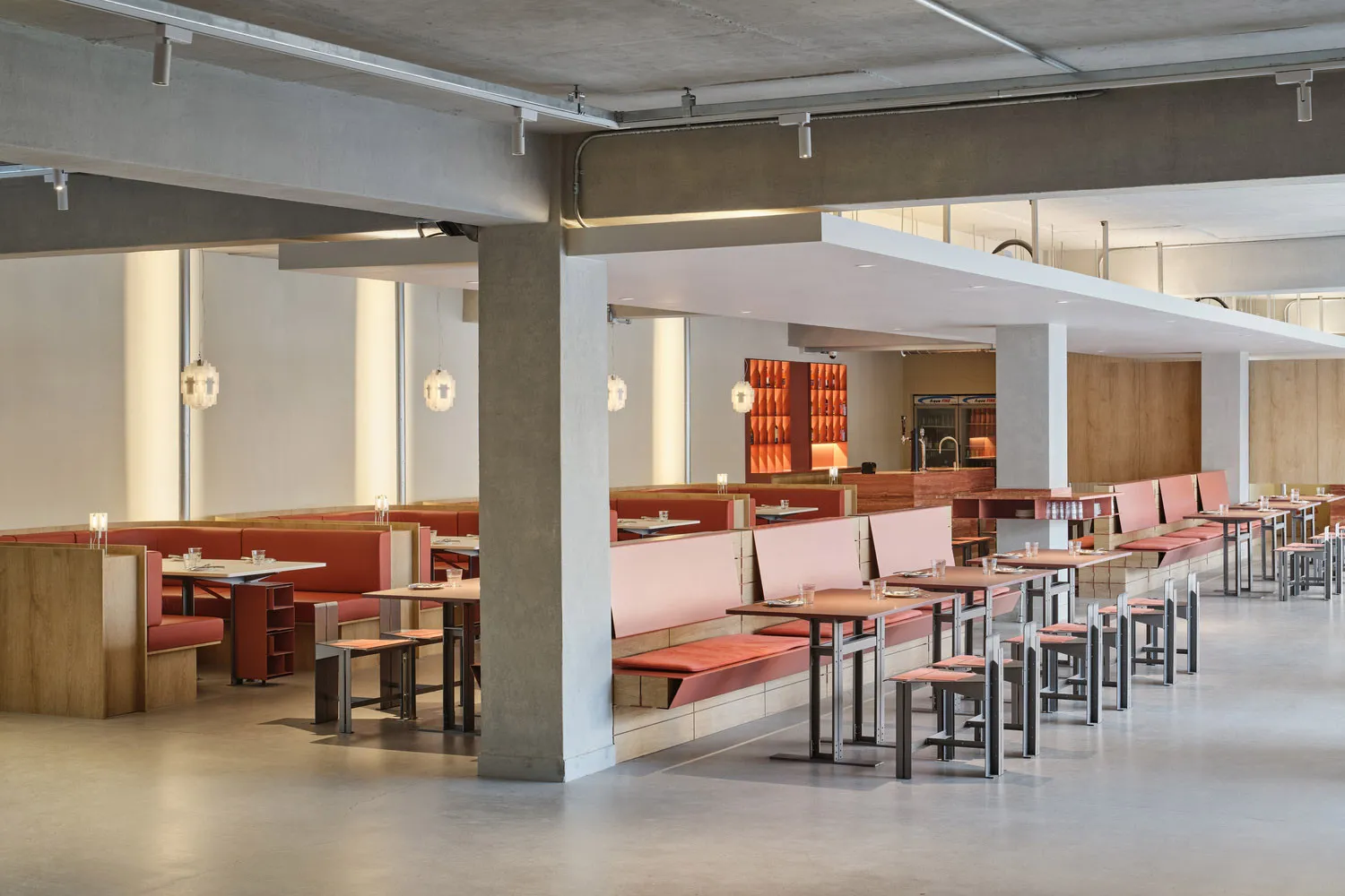 A well-designed modern restaurant with exposed concrete ceiling, red seats, and metallic tables.