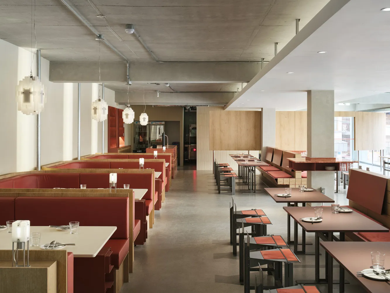 A spacious restaurant interior with modern design elements, including red upholstered booths and a concrete ceiling.