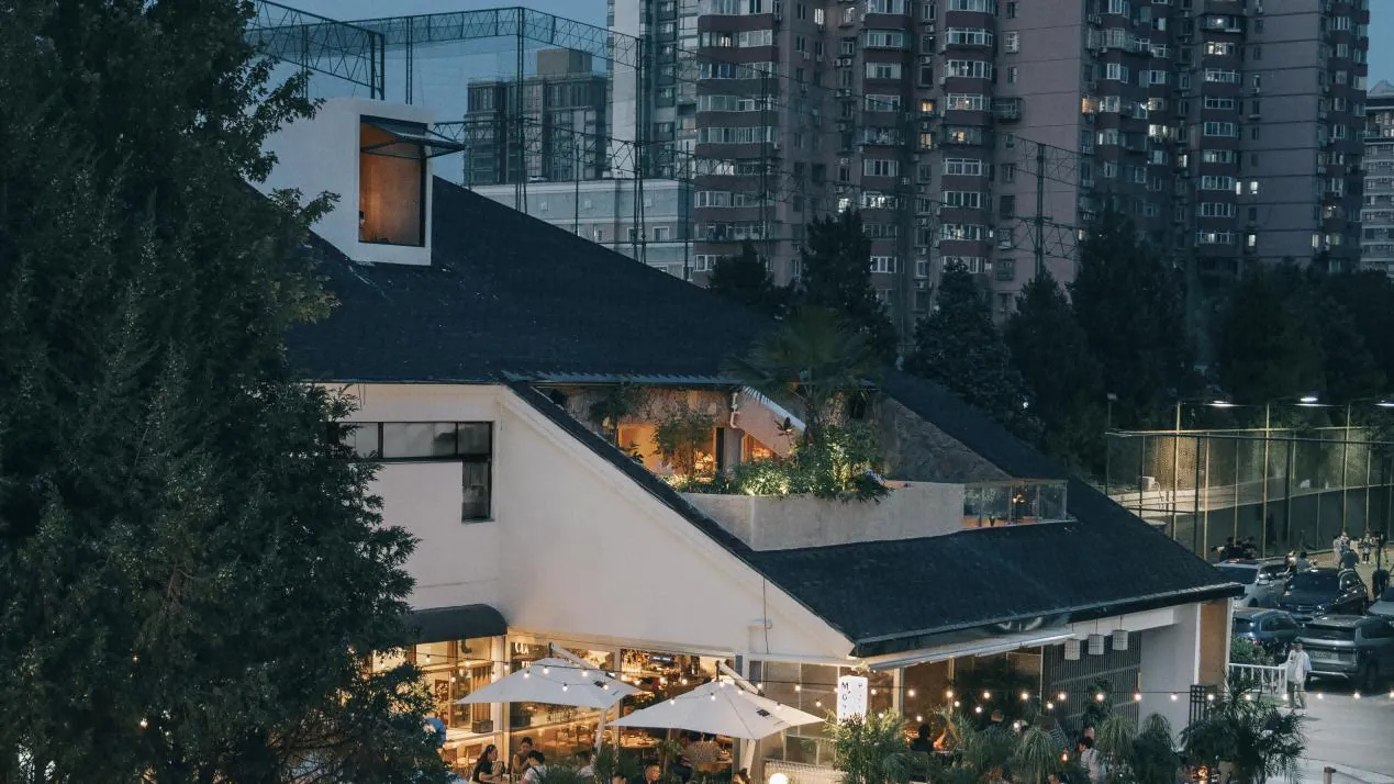 一座現代餐廳外觀,擁有混凝土牆面與屋頂花園,周圍環繞高樓與樹木。