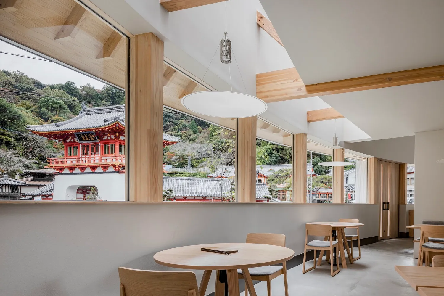 Modern cafe interior with wooden furniture and architectural details overlooking a traditional Japanese temple.