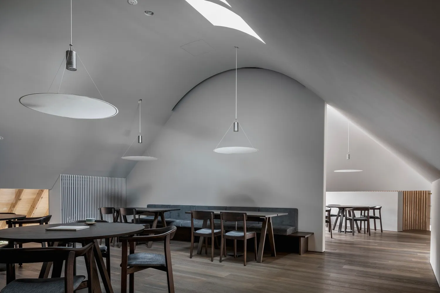 A minimalist restaurant interior with gray walls, wooden tables, and pendant lights.