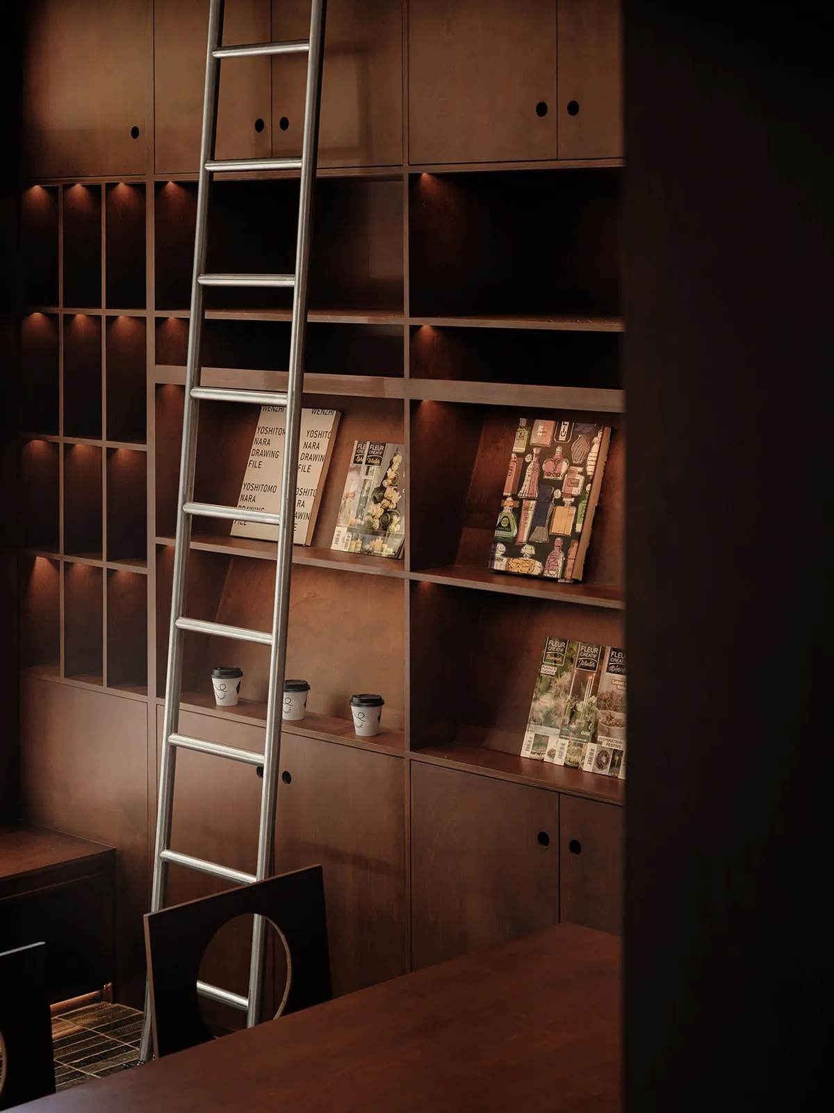 A modern library with wooden bookshelves and a ladder for accessing the higher shelves.