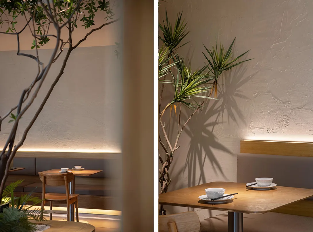 A serene restaurant interior featuring modern design elements like wood, concrete, and lush green plants.