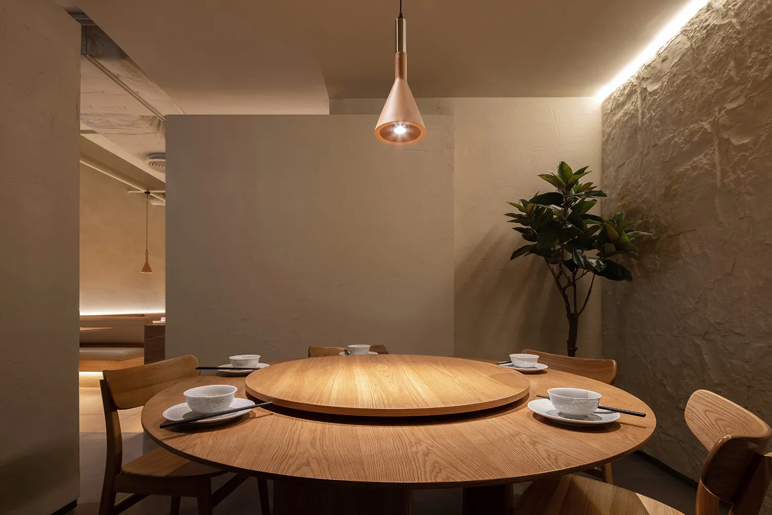 A round dining table in a modern restaurant interior, surrounded by wooden chairs and featuring a central lazy susan.