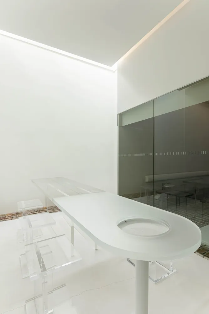 A modern minimalist bar counter with a frosted glass surface and transparent stools.