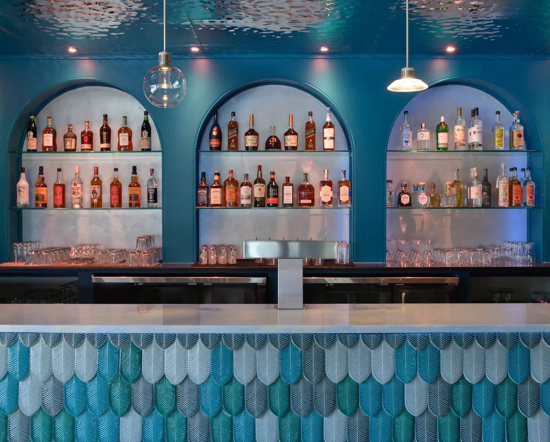 A photograph of a modern bar counter featuring glass shelves with various bottles of liquor.