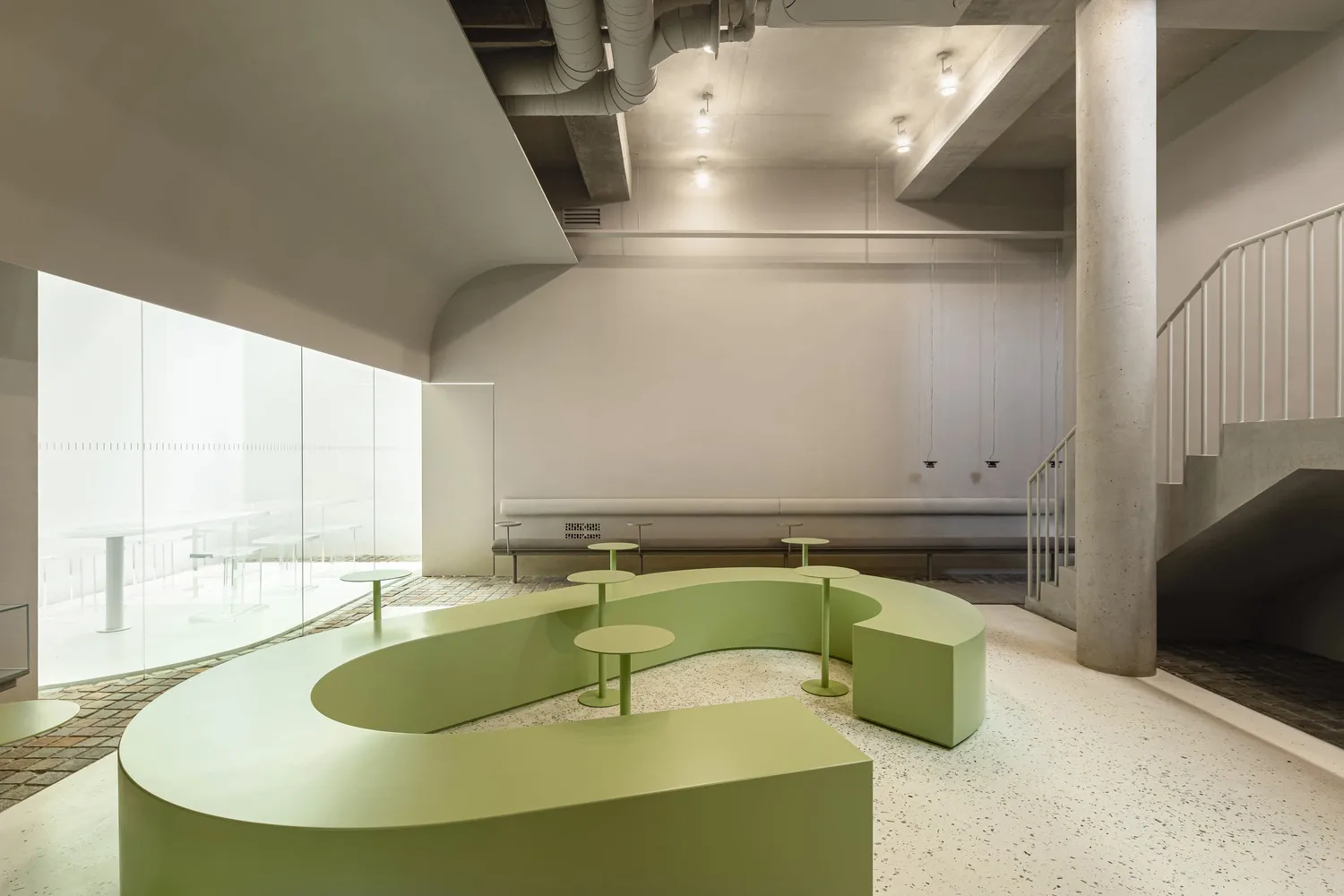 A modern cafe interior with green seating and concrete elements.
