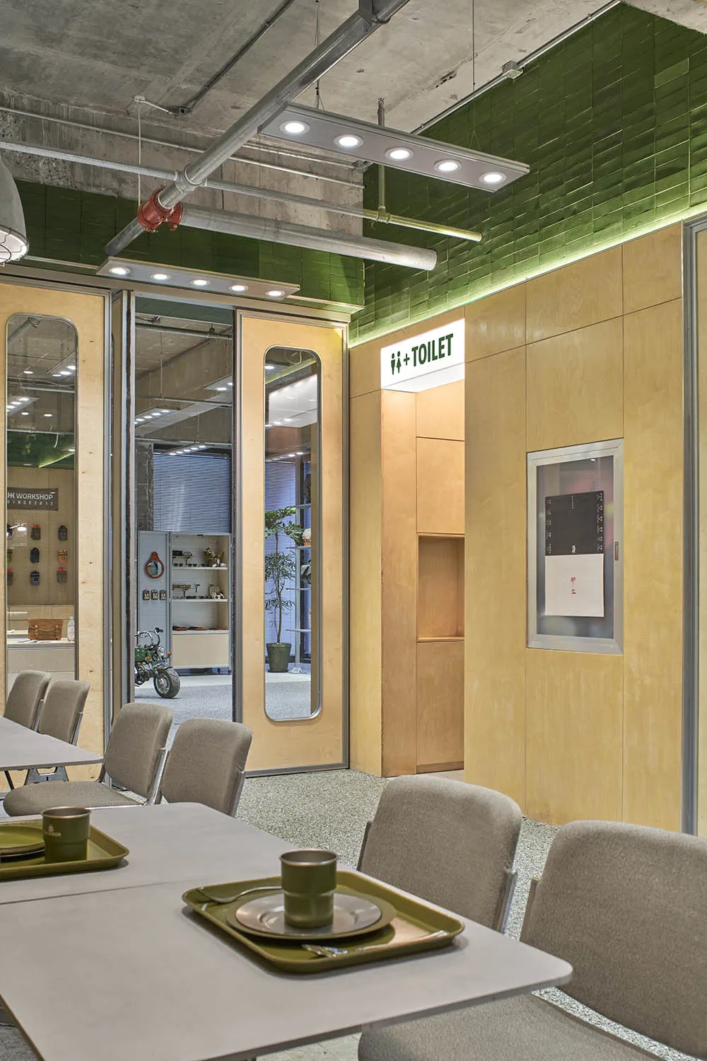 An industrial-style cafe with green tiled walls, concrete ceiling, and wooden paneling, featuring a modern table setting with
