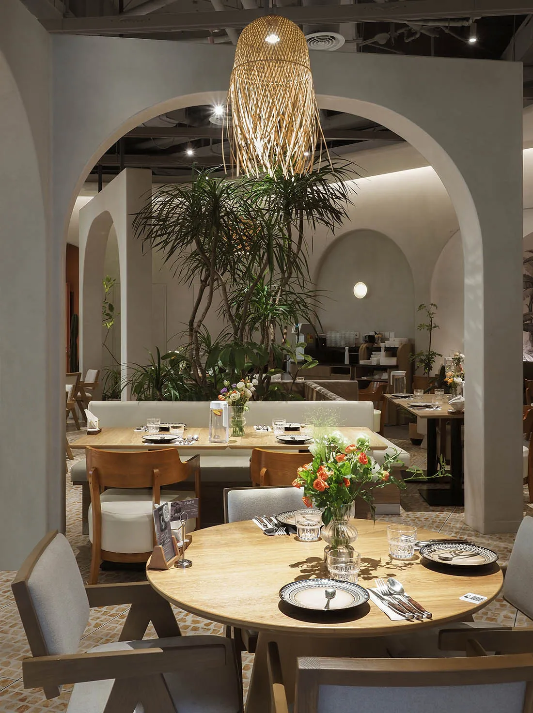 Modern restaurant interior with wooden tables, glass vases, and plush fabric chairs.