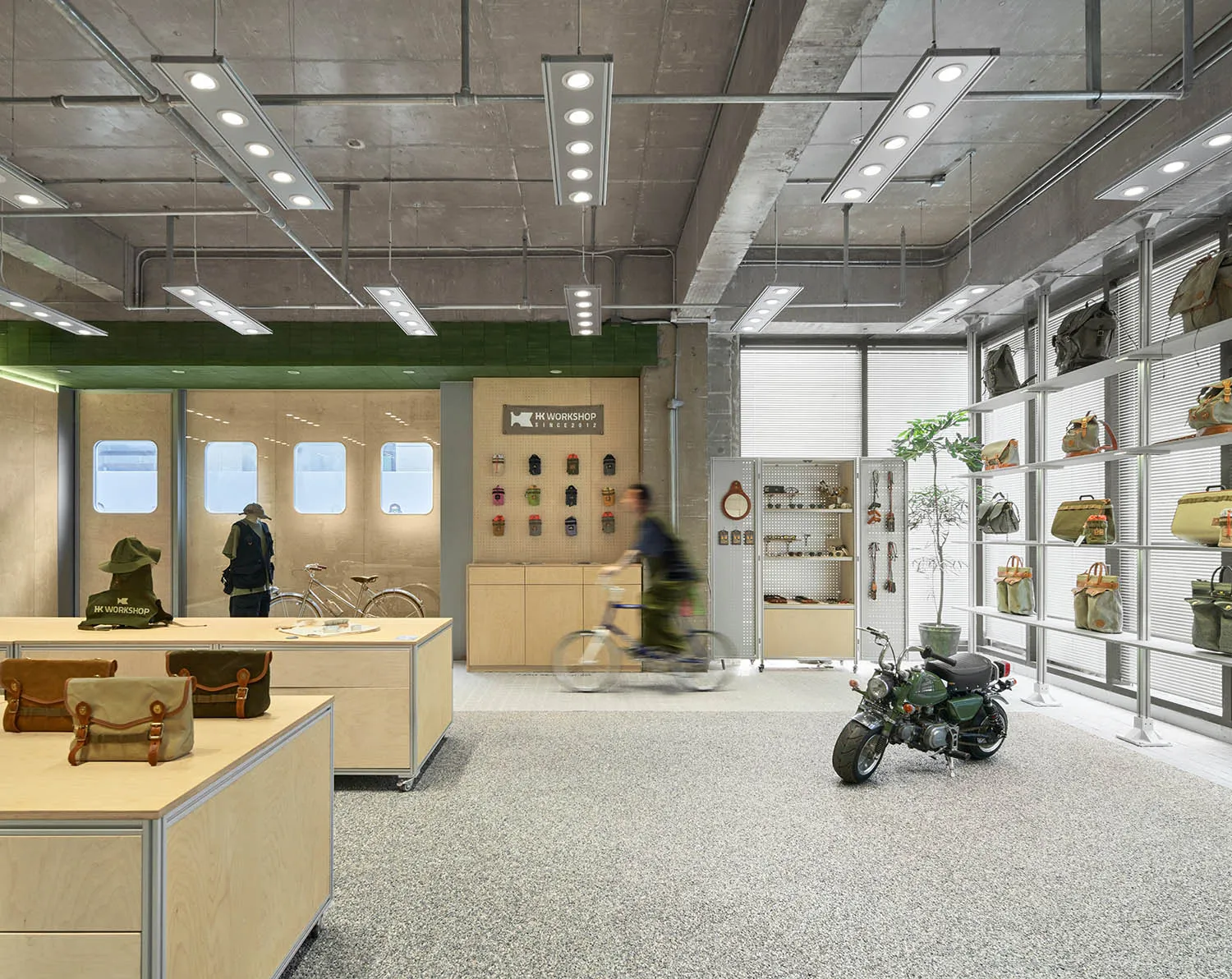 A modern retail store with concrete walls, metal shelving, and wood accents displaying various bags and accessories.