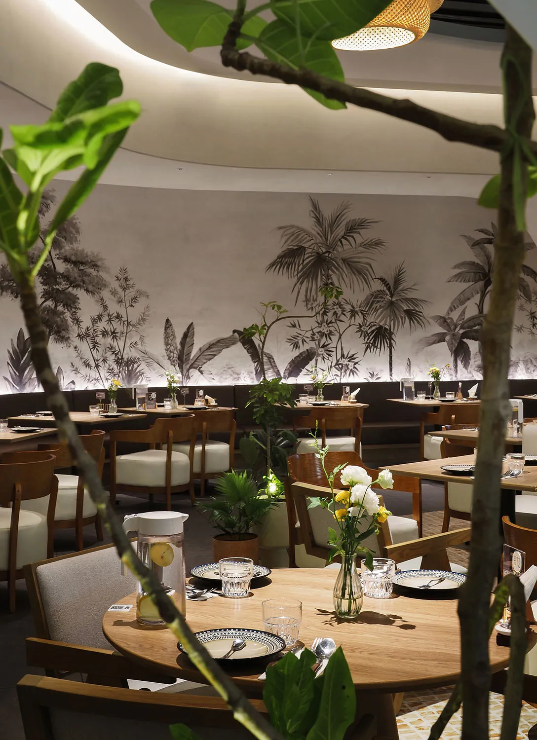 Lushly decorated cafe with wooden furniture and plant life on tables and walls.