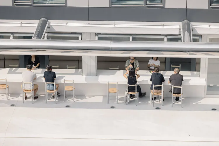 Group of people sitting at a modern, minimalist public space with concrete seating and minimalist design.