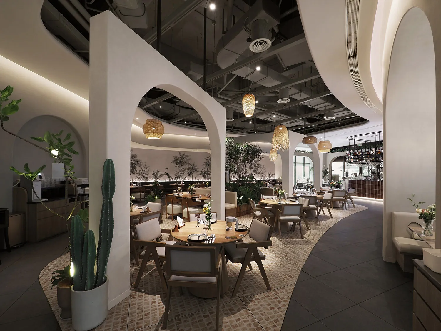 A modern restaurant interior with cement walls, wooden tables, and greenery.