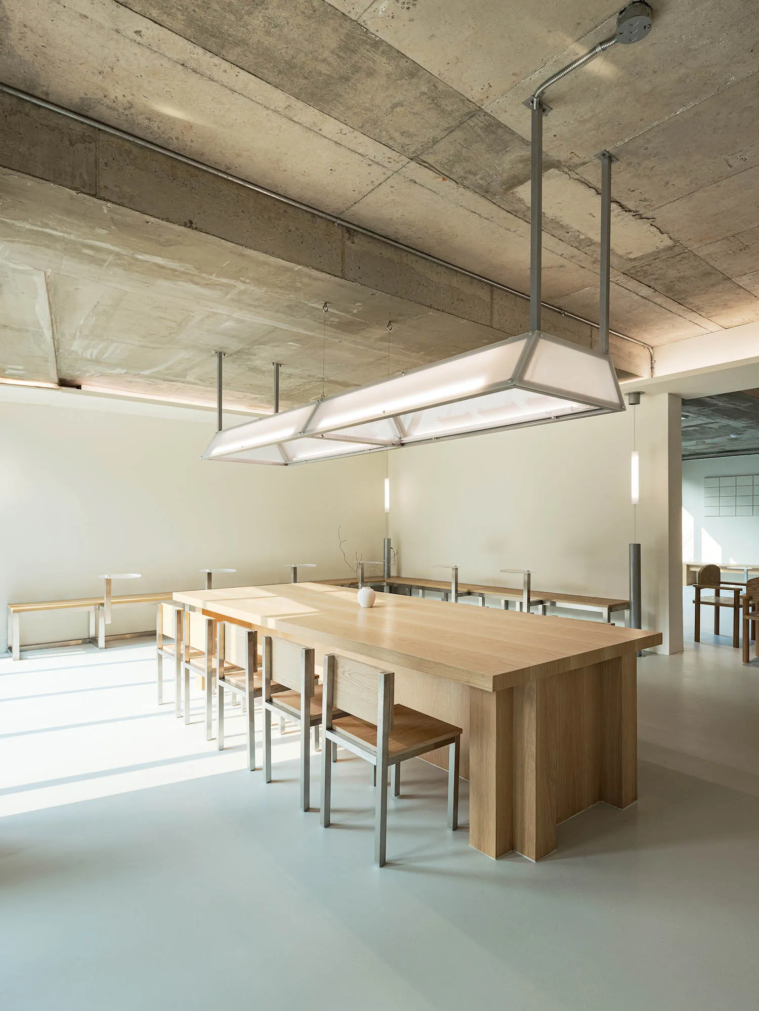Modern restaurant interior with minimalist design featuring wood tables, metal chairs, and concrete ceiling.