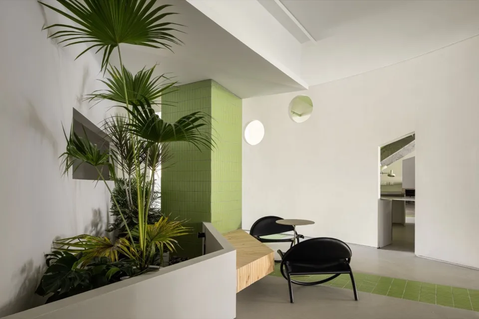 Modern lobby interior with concrete walls, green tiled wall, and seating area with black chairs.
