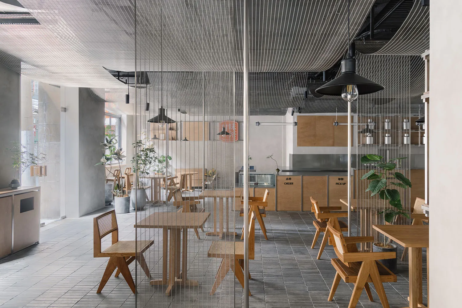 Modern restaurant interior featuring wooden tables and chairs, concrete floors, and industrial lighting.