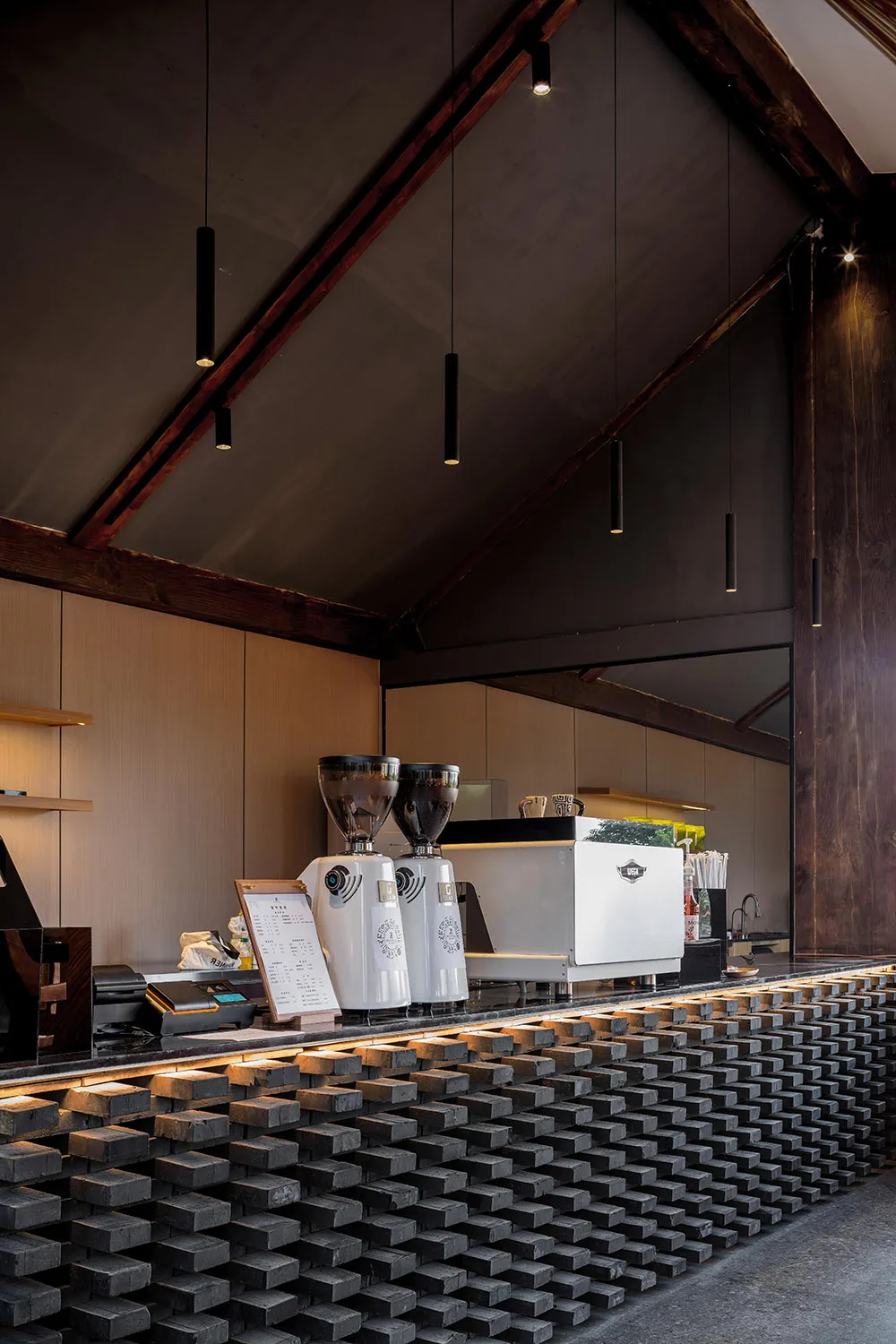 A modern coffee shop counter with metal elements and a brick-like pattern on the floor.