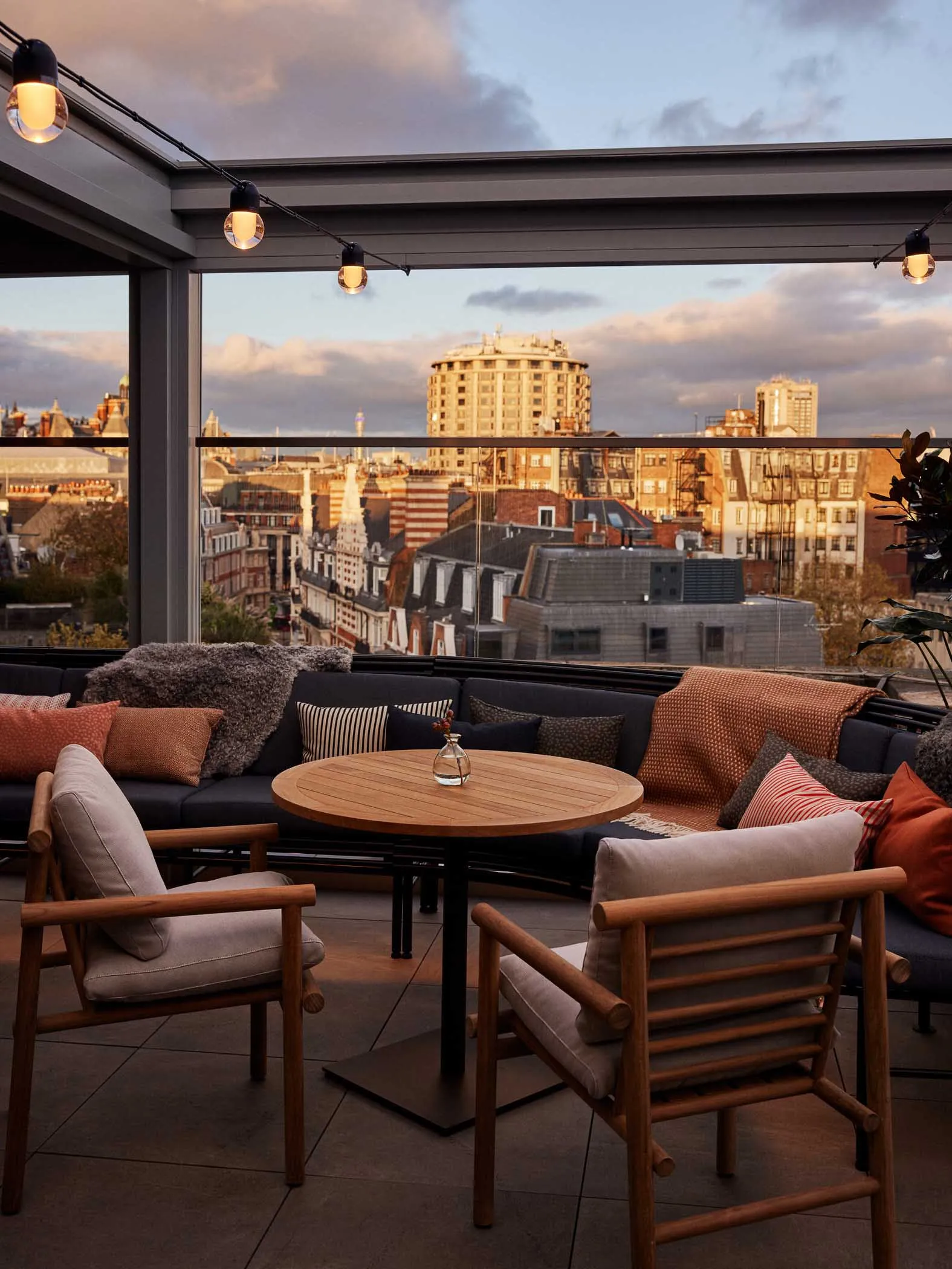 A cozy rooftop lounge with plush seating and warm lighting, overlooking a cityscape.
