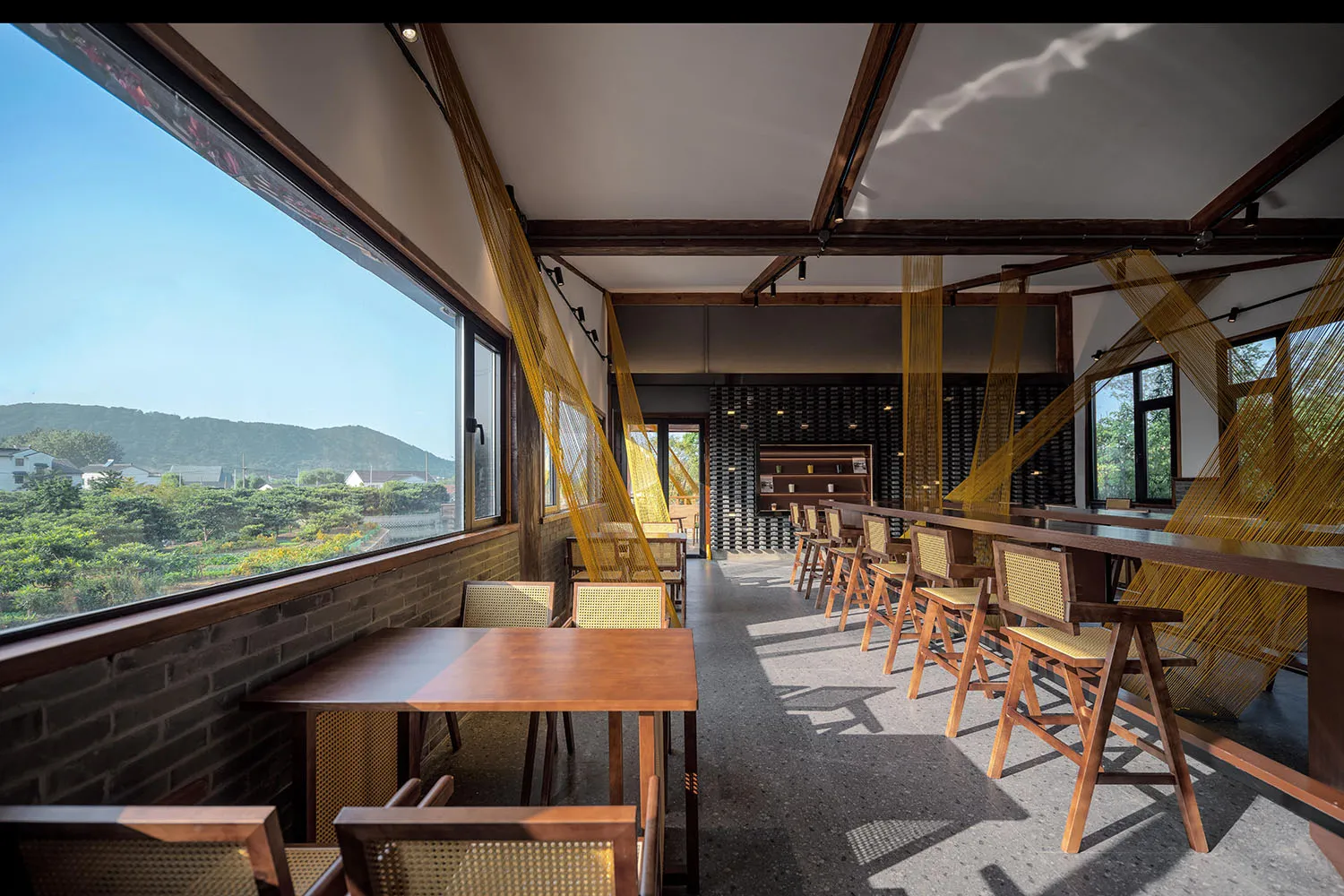 Modern cafe interior with wooden tables and glass walls, overlooking scenic landscape.