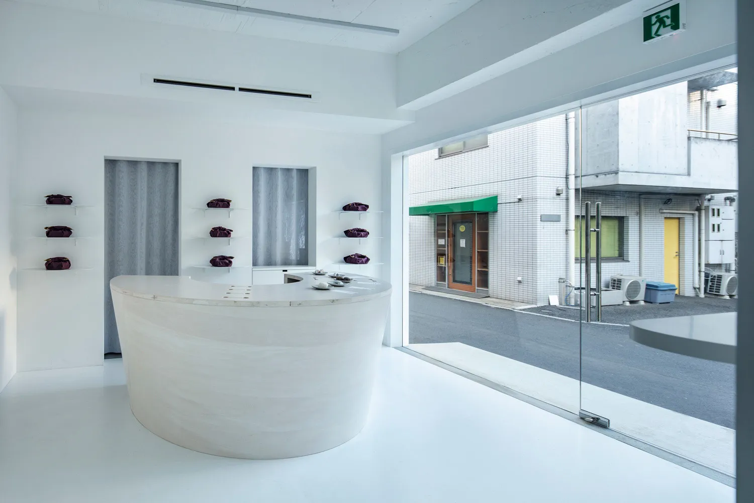A minimalist retail storefront with a large, curved white marble reception desk and purple bags displayed on shelves against 