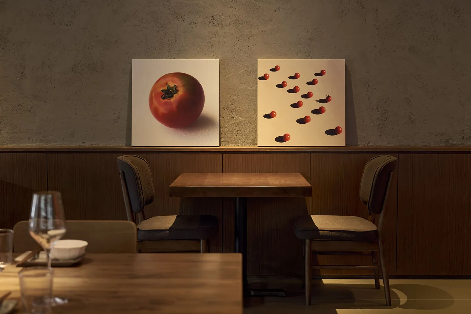 A restaurant interior with a wooden table and two paintings featuring tomatoes.