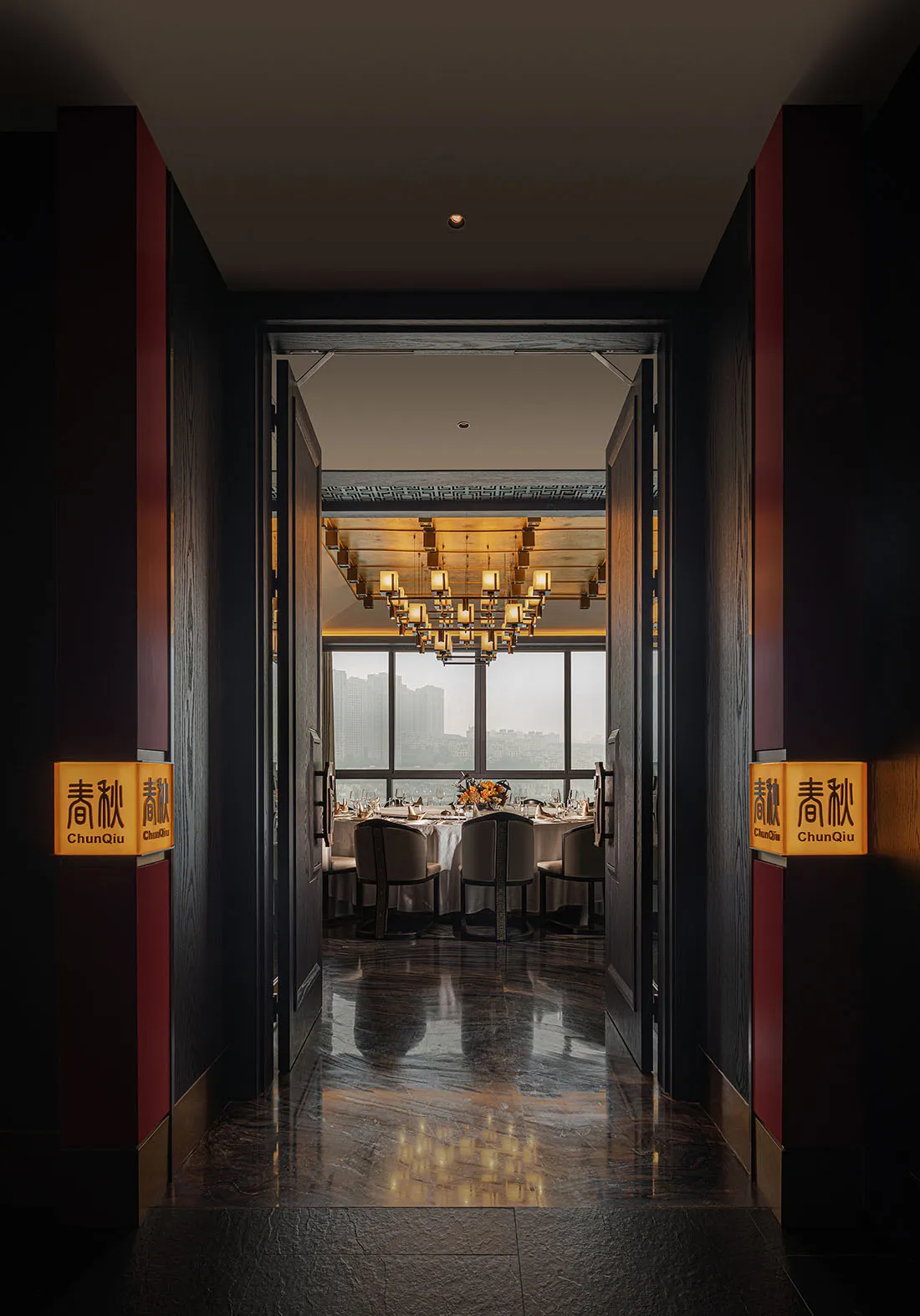 Modern, industrial-themed restaurant interior with marble flooring, large windows overlooking a cityscape, and a warm, inviti
