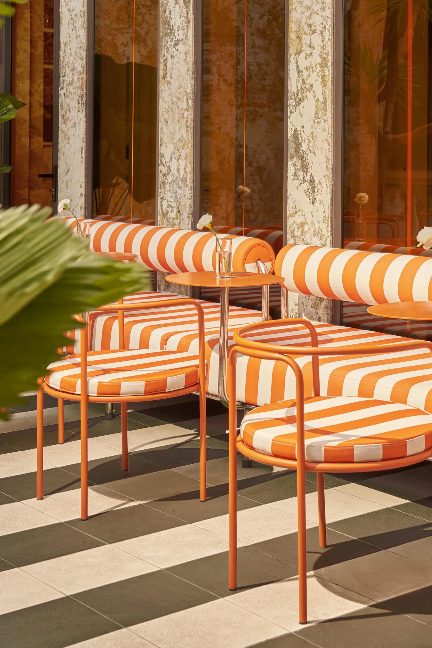 A café seating area with orange and white striped seats and metal frames, with a small round table and a plant in the foregro