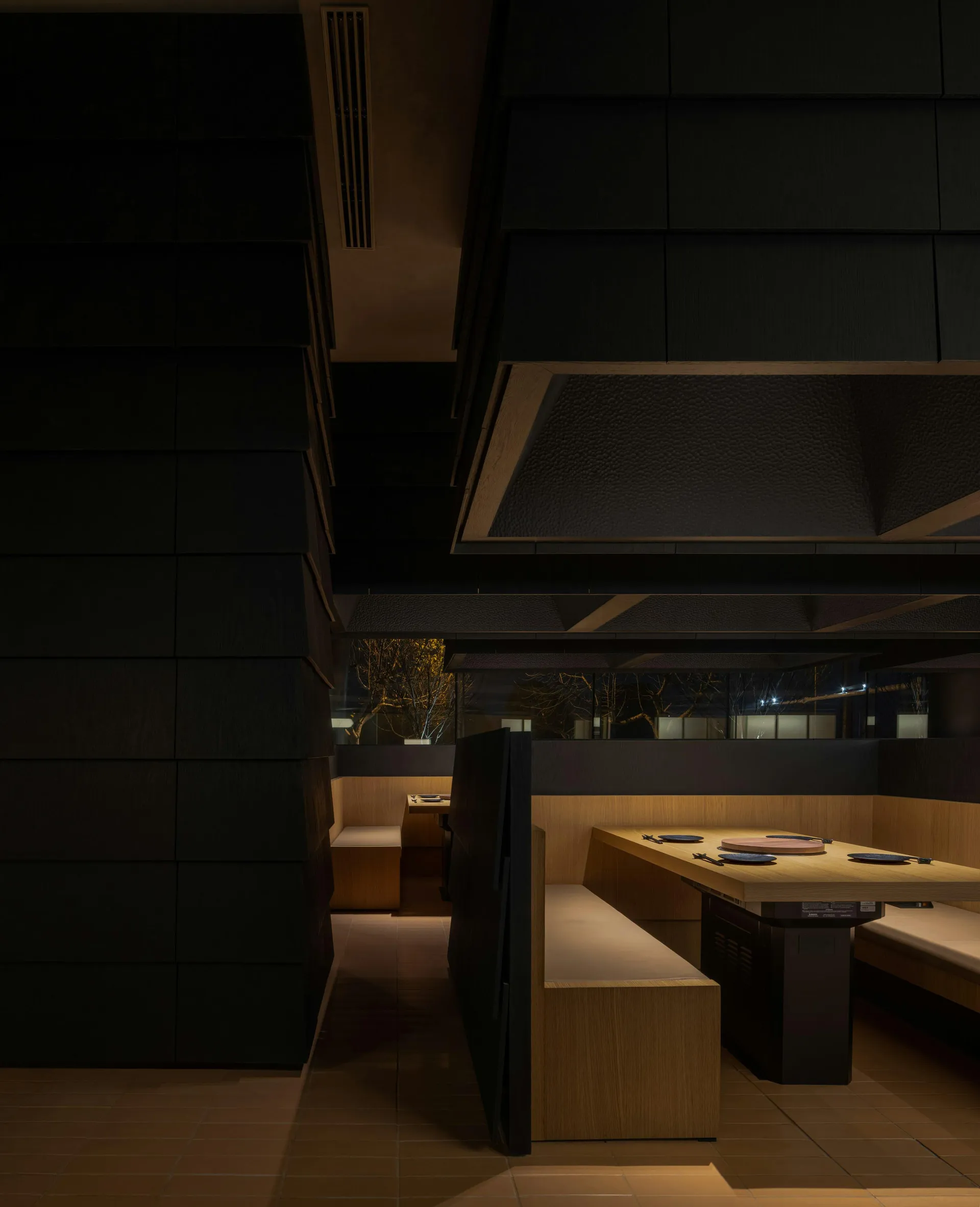 Dark, minimalist restaurant interior with wooden seating and lighting.