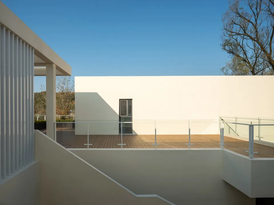 A minimalist modern rooftop deck with wooden flooring and white walls, under a clear blue sky.