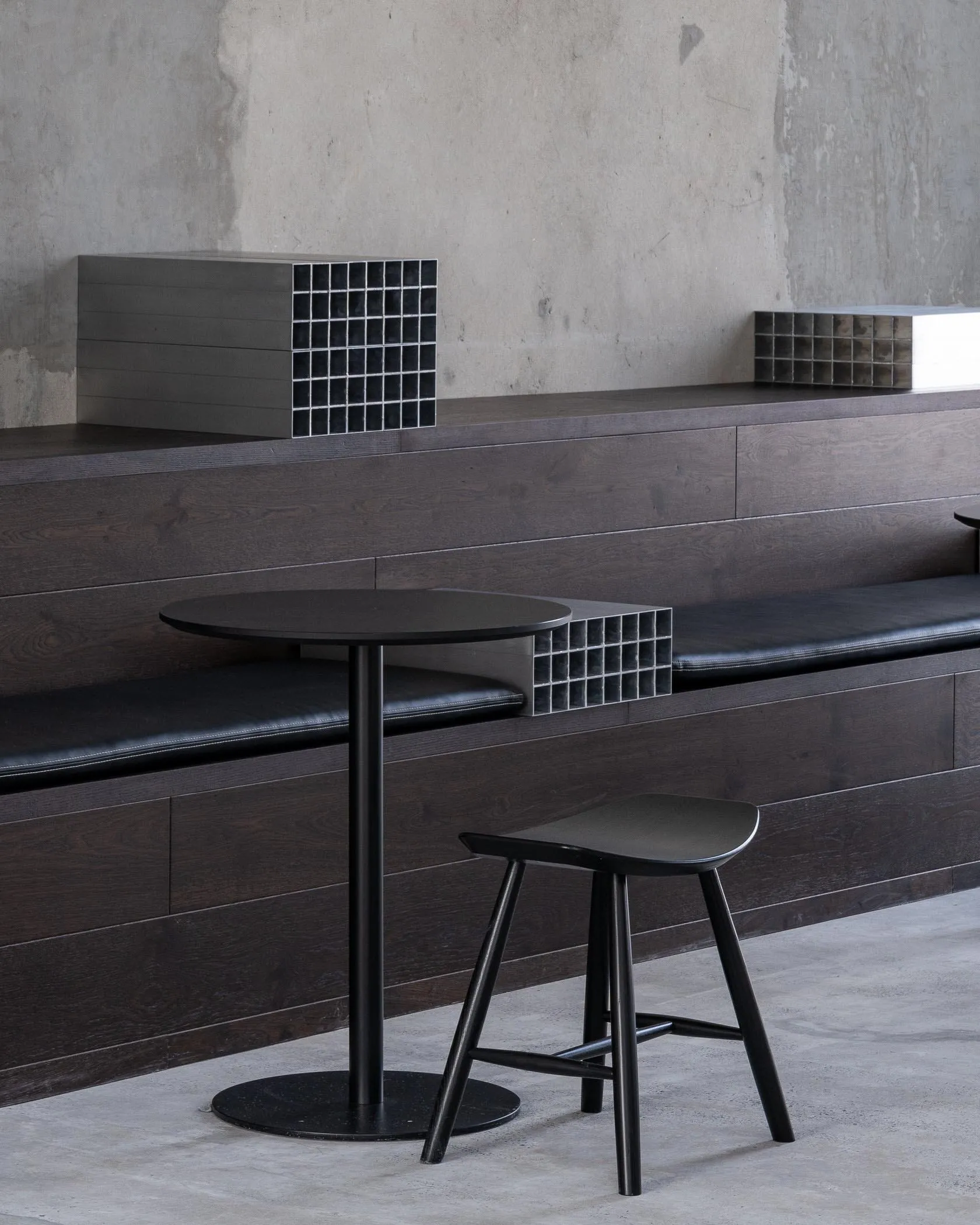 Industrial-style coffee shop interior with modern furniture, including a round black table, a black bar stool, and a built-in