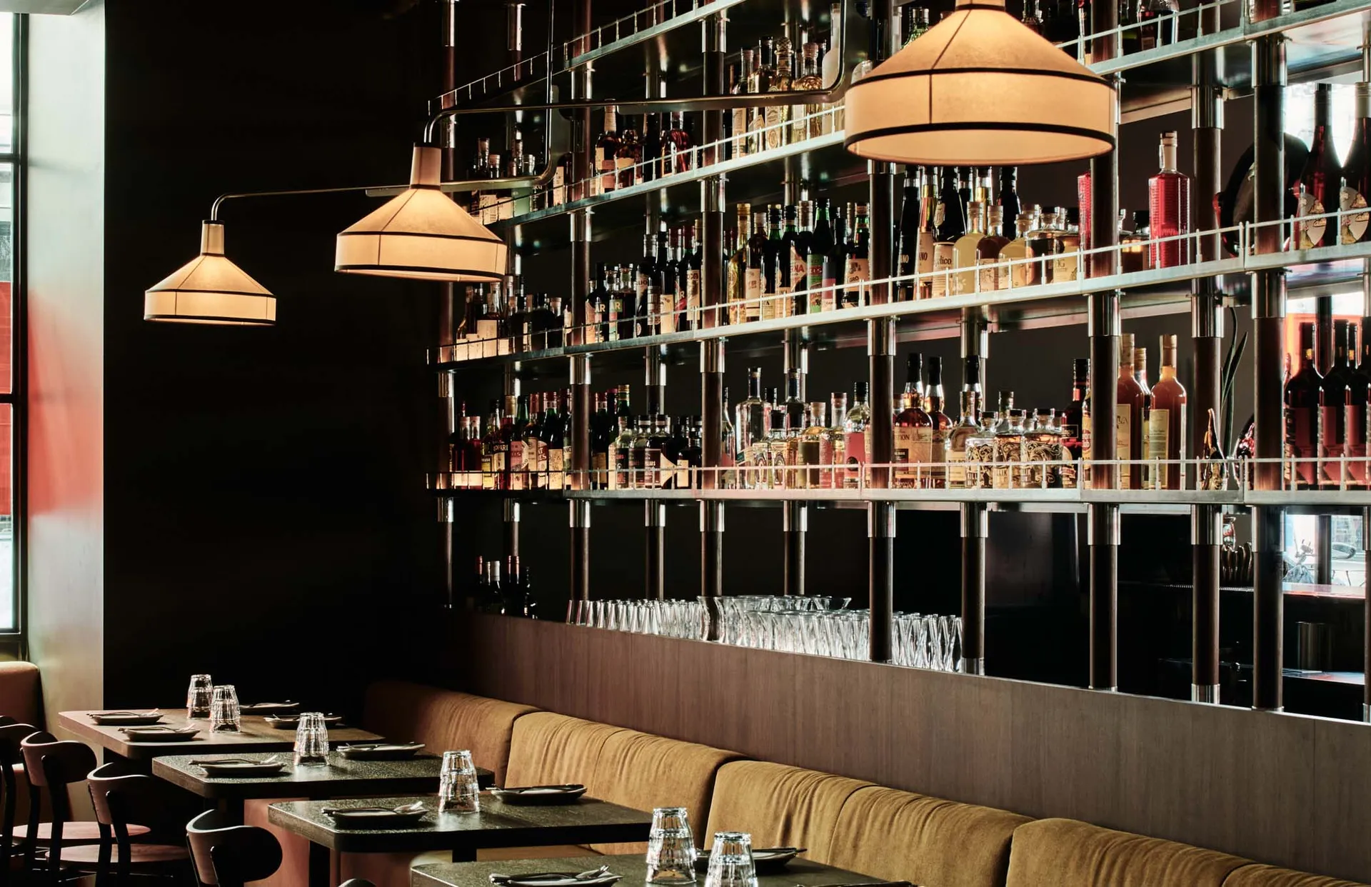 Modern restaurant bar with a metal shelving system displaying an extensive selection of glassware and bottles.