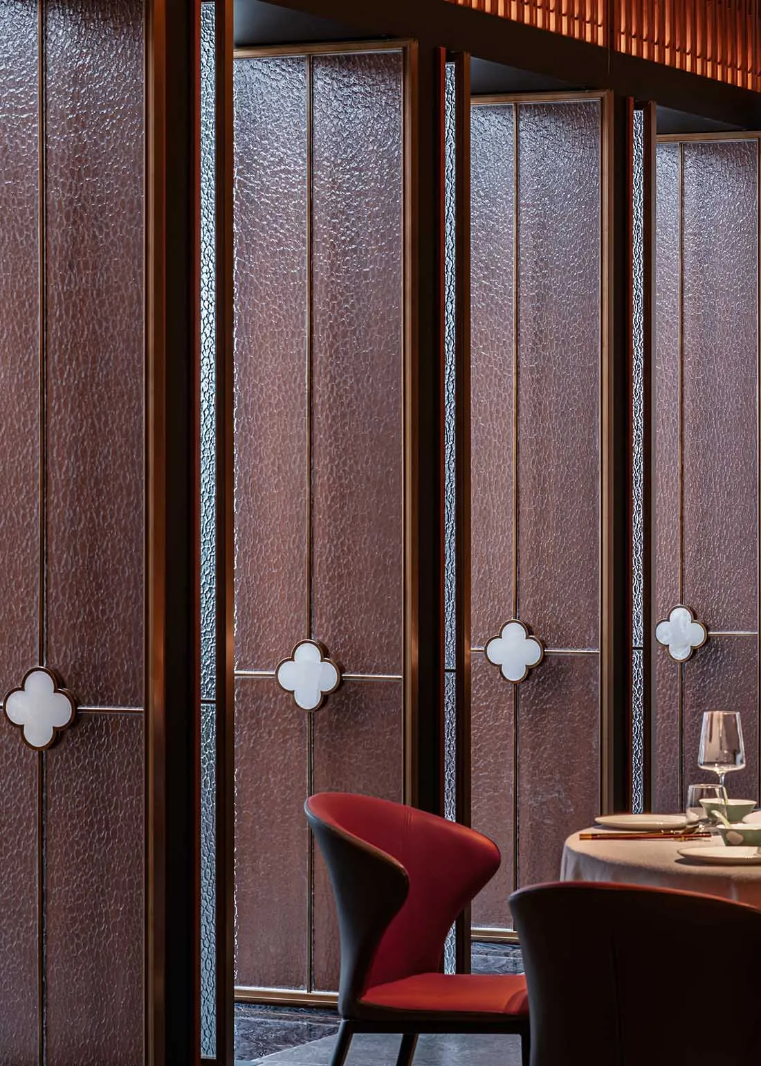 A modern restaurant interior featuring glazed glass panels and a red upholstered chair.