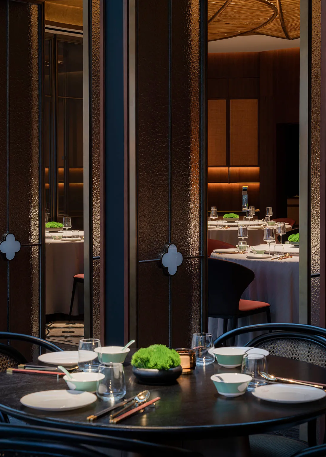 A modern restaurant interior with black and white tables, wooden accents, and greenery.