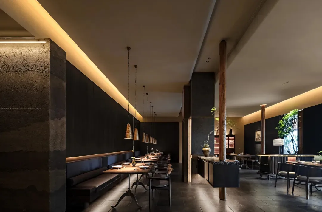 Modern restaurant interior with concrete walls, wooden tables, and metal pendant lights.