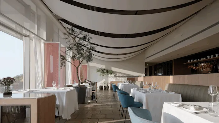 Modern restaurant interior with white tablecloths, blue chairs, white tables, brown flooring, green plants, black vertical st